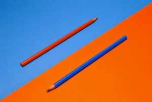photo split diagonally with red pencil on blue background and blue pencil on red background