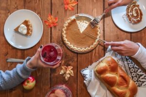 Picture of a Thanksgiving scene with a table that has pumpkin pie, bread, and drinks being passed around