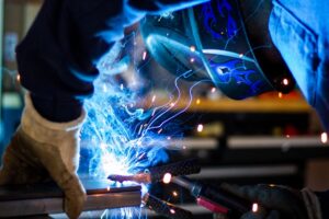 image of a manufacturing worker welding metal accompanied by sparks and smoke