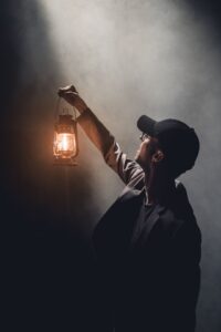 Man holds lit lantern in dark to guide