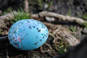 Sparkly blue Easter egg sitting on the ground outside